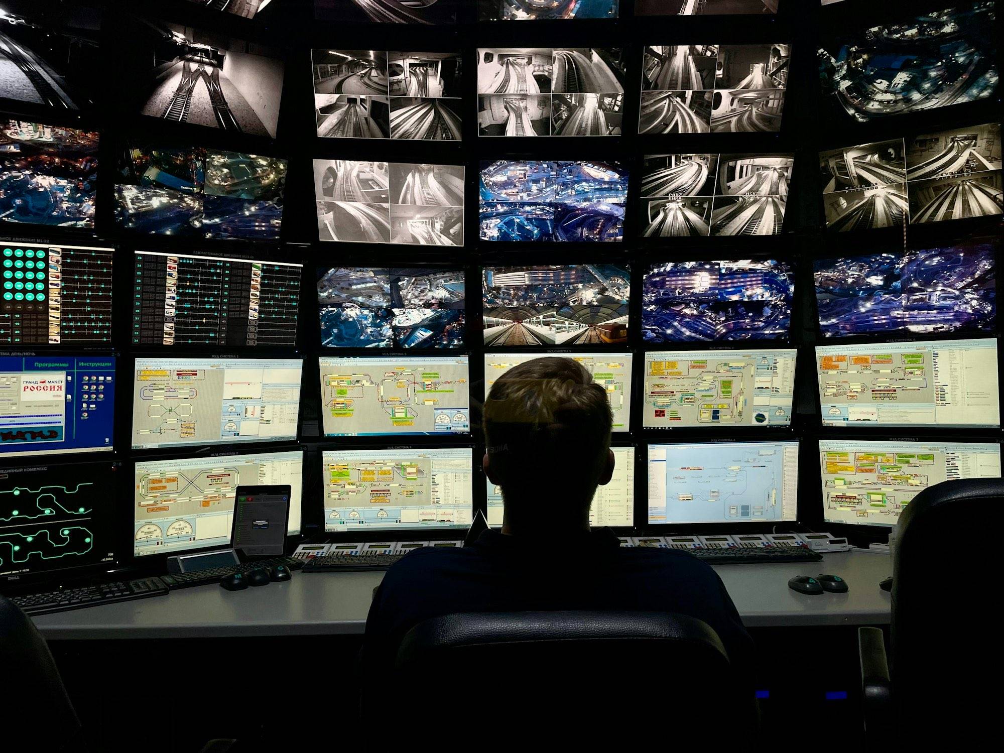 An analyst reviewing a wall of monitoring screens in a dark operations room